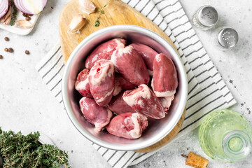 Raw turkey hearts in a metal bowl on a light gray table. Top view
