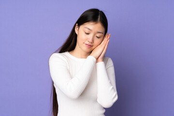 Young asian woman isolated on purple background making sleep gesture in dorable expression