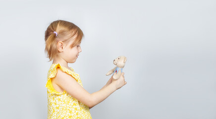 Little Caucasian girl with teddy bear standing sideways to the camera