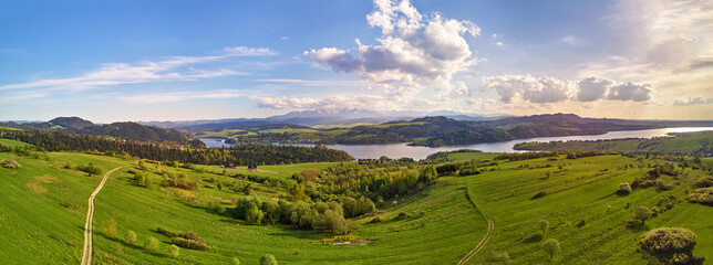 Spring mountain panorama. Lake Czorsztyn on Dunajec river. Village in green forest and meadow hills. - 421782764