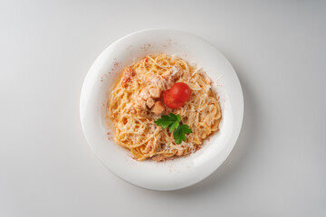 Pasta with salmon in a white plate decorated with tomatoes and herbs top view