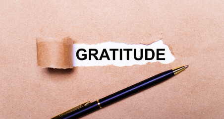 Torn kraft paper, white background with the text GRATITUDE. Nearby is a black handle. View from...