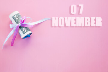 calendar date on pink background with rolled up dollar bills pinned by pink and blue ribbon with copy space.  November 7 is the seventh day of the month