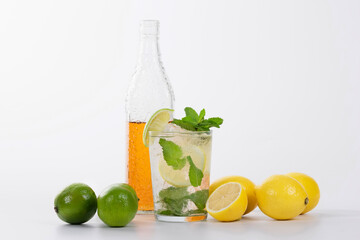 view of a mojito cocktail surrounded by lemons, limes and a half full glass bottle