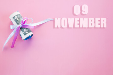 calendar date on pink background with rolled up dollar bills pinned by pink and blue ribbon with copy space. November 9 is the ninth day of the month