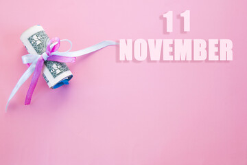 calendar date on pink background with rolled up dollar bills pinned by pink and blue ribbon with copy space. November 11 is the eleventh day of the month