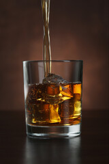 Pouring whiskey into glass with ice cubes on table