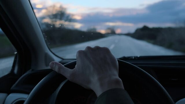First person view of driving a car on countryside road during evening and overcast weather. Hand on steering wheel view.