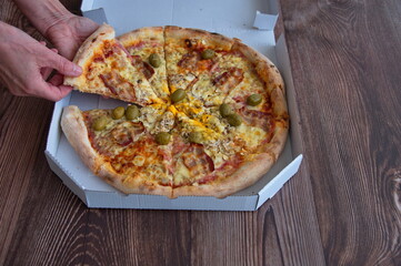 Delicious takeout pizza on a wooden table. Cropped photo of hands taking piece of pizza