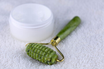 A roller for massage with jade stones for the face and a jar of cream.