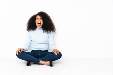 Young african american woman sitting on the floor shouting to the front with mouth wide open