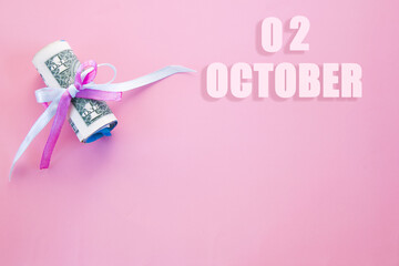 calendar date on pink background with rolled up dollar bills pinned by pink and blue ribbon with copy space. October 2 is the second day of the month