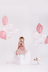 happy birthday 2 years old little girl in pink dress. white cake with candles and roses. Birthday decorations with white and pink color balloons and confetti for party on a white wall. Happy birthday