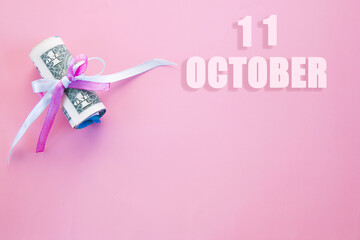 calendar date on pink background with rolled up dollar bills pinned by pink and blue ribbon with copy space. October 11 is the eleventh day of the month