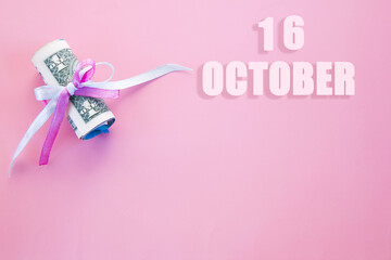 calendar date on pink background with rolled up dollar bills pinned by pink and blue ribbon with copy space. October 16 is the sixteenth day of the month