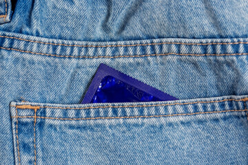 Close-up of a pocket of blue jeans from which a condom sticks out