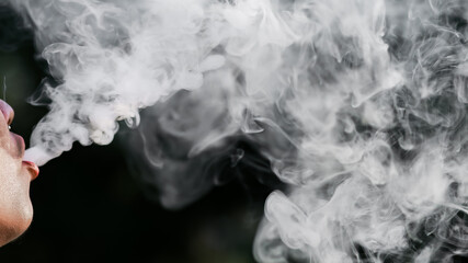 Close-up of a man spewing cigarette smoke from his mouth, black background, and space for text.