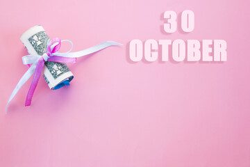 calendar date on pink background with rolled up dollar bills pinned by pink and blue ribbon with copy space. October 30 is the thirtieth day of the month