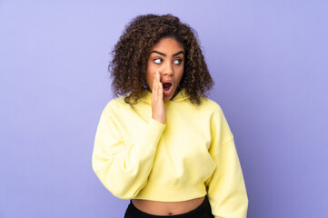 Young African American woman isolated on background whispering something with surprise gesture while looking to the side