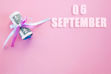calendar date on pink background with rolled up dollar bills pinned by pink and blue ribbon with copy space. September 6 is the sixth day of the month