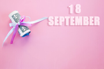 calendar date on pink background with rolled up dollar bills pinned by pink and blue ribbon with copy space. September 18 is the eighteenth day of the month