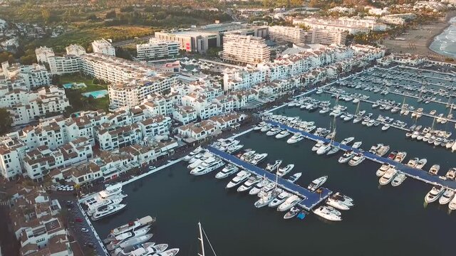Panoramic aerial perspective of luxury Pueto Banus Bay. Exclusive area of Marbella. Famous location for expensive lifestyle , luxury yacht. Drone forward and tilt up. Golden hour with warm 