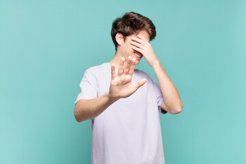 young boy covering face with hand and putting other hand up front to stop camera, refusing photos...