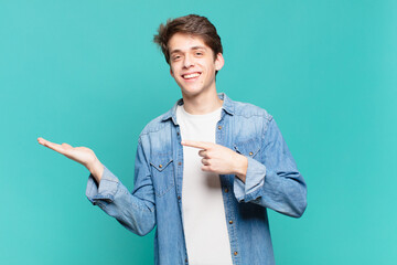 young boy smiling cheerfully and pointing to copy space on palm on the side, showing or advertising an object © kues1