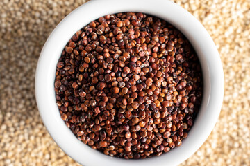 Red quinoa in white bowl on white quinoa, top view
