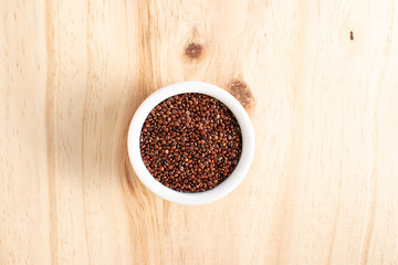 Red quinoa in white bowl on wood