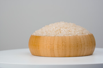 Rice in a wooden bowl. Raw rice grains on white background. Rice grains in wooden container.  Free place for text.  
Marketing, advertising use. 