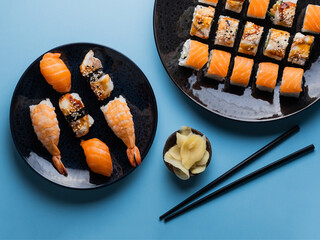 Delicious appetizing sushi set, served on clay plate with soy sauce and chopsticks, flat lay on blue table. Traditional Japanese food, tasty seafood, sushi restaurant concept