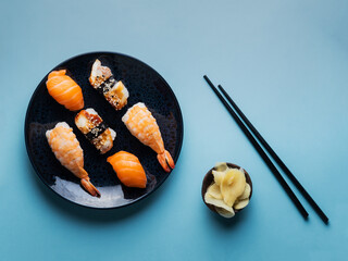 Delicious appetizing sushi set, served on clay plate with soy sauce and chopsticks, flat lay on blue table. Traditional Japanese food, tasty seafood, sushi restaurant concept