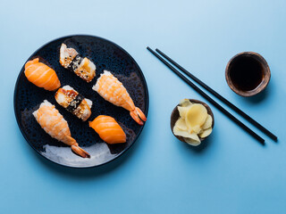 Delicious appetizing sushi set, served on clay plate with soy sauce and chopsticks, flat lay on blue table. Traditional Japanese food, tasty seafood, sushi restaurant concept