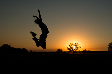 Obraz na płótnie Canvas silhouette of a girl jumping up against the background of the sun setting over the horizon