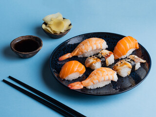 Delicious appetizing sushi set, served on clay plate with soy sauce and chopsticks, flat lay on blue table. Traditional Japanese food, tasty seafood, sushi restaurant concept