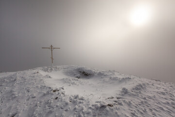Misty snow-covered mountain with cross and sunlight