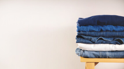 Clothes Concept. Stack of Clothing on Wooden bench by the Whaite Wall. Blue Navy Tone