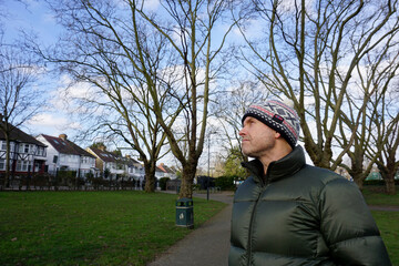 Portrait half body of handsome good looking Caucasian man  wearing green jacket, bobble hat with white pom pom stand looking up the blue sky in the park 
