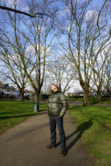 Portrait full body of handsome Caucasian man  wearing green jacket, bobble hat with white pom pom stand looking up the blue sky in the park 