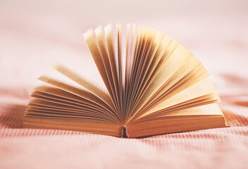 An interesting old book with yellowed pages lies open on the bed with a pink striped blanket. Pastime and self-development.