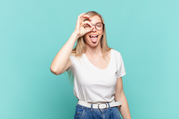young blond pretty woman smiling happily with funny face, joking and looking through peephole,...