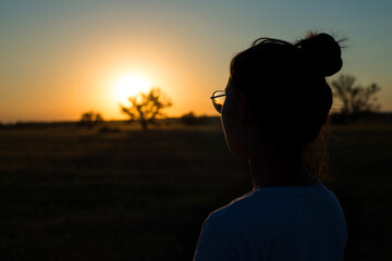the silhouette of a girl looking at the sun setting over the horizon