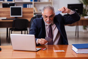 Old male employee playing cards at workplace