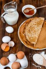 ingredients for making pancakes. flour, eggs, milk, honey. fresh thin pancakes on a wooden table 