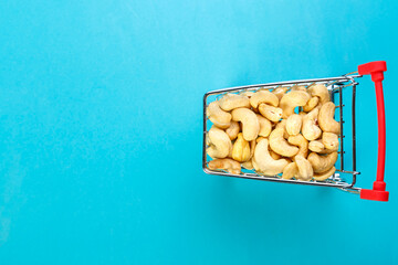 Food cart filled with peeled cashews on a blue background. Copy space.