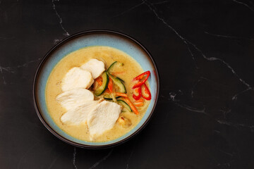 Asian soup with chicken and vegetables: zucchini, red pepper and carrot. Dish isolated in a blue bowl, close-up on a black marble background. Asian cuisine.