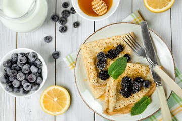 fresh thin pancakes with berries, honey and powdered sugar on a wooden table. delicious sweet breakfast. 