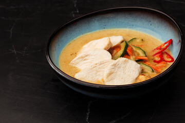 Asian soup with chicken and vegetables: zucchini, red pepper and carrot. Dish isolated in a blue bowl, close-up on a black marble background. Asian cuisine.