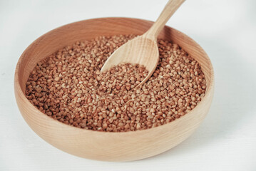 Buckwheat kernels in wooden bowl and spoon on white background. Top view. Copy, empty space for text